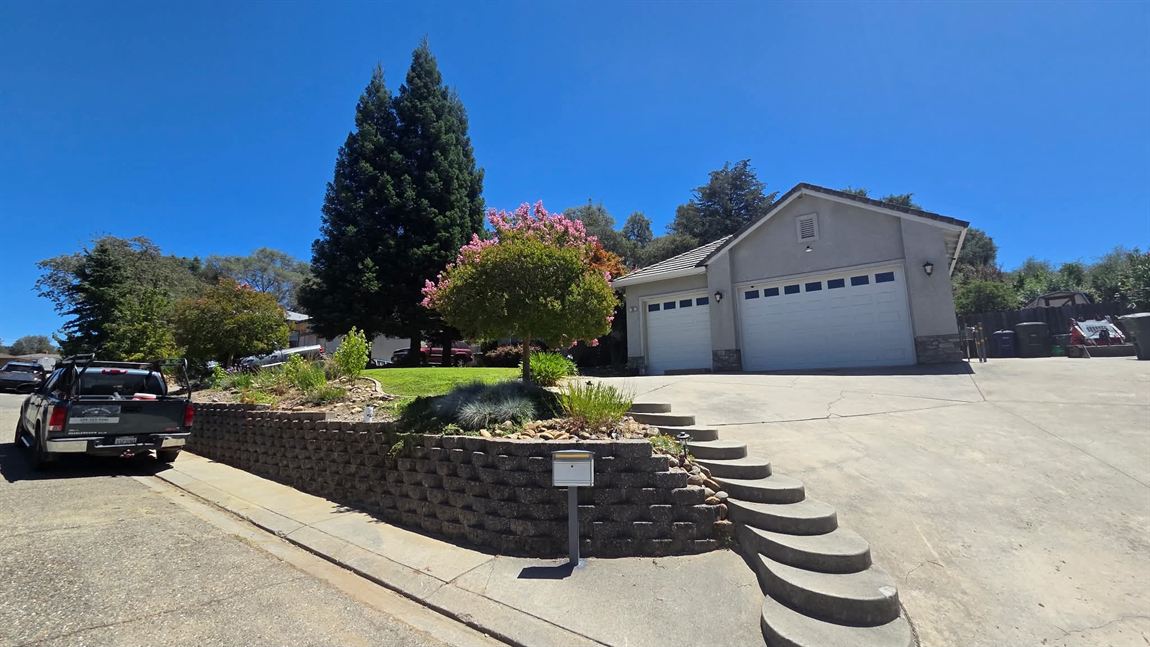 Curved segmental block retaining wall terracing a front yard up to a two-car garage, planted above with a flowering crape myrtle, ornamental grasses and shrubs